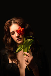 Close-up of woman holding flower against black background