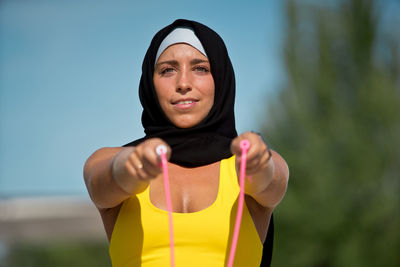 Portrait of smiling woman using skipping rope outdoors