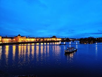 Illuminated city by river against sky at dusk