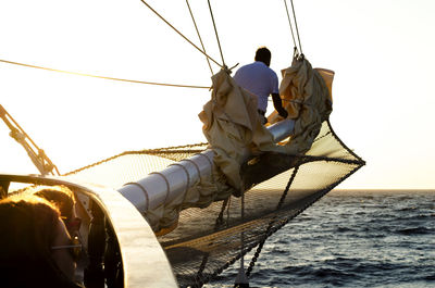 Rear view of men fishing in sea against clear sky