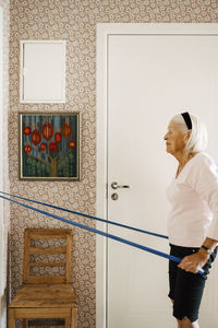 Side view of senior woman pulling resistance band while exercising at home