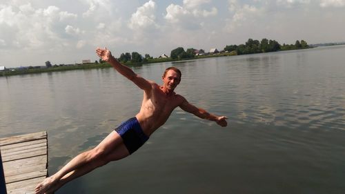 Full length portrait of shirtless man with arms outstretched diving in lake against sky