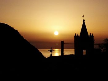 Silhouette temple by sea against sky during sunset