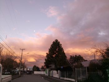 Road by trees against sky at sunset