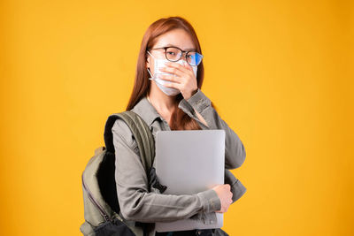 Portrait of smiling woman using smart phone against yellow background