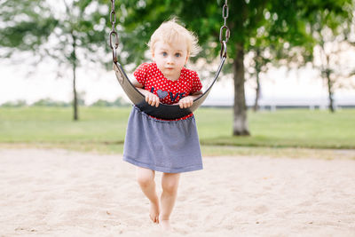 Full length portrait of cute girl leaning on swing over sand