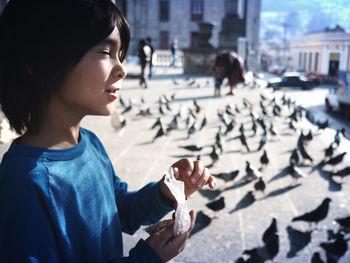 Boy feeding flock of pigeons on sidewalk