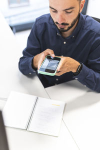 Young businessman photographing through smart phone at desk