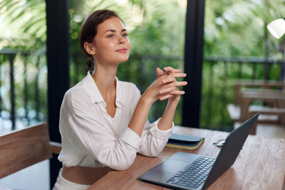 Portrait of smiling woman using laptop while sitting on table