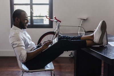 Man using laptop in home office with feet on desk