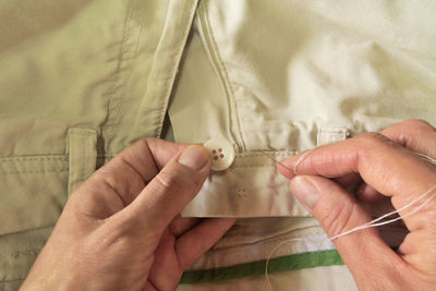Close-up of human hand stitching button of pant