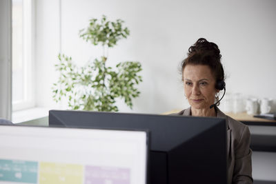 Smiling mature businesswoman using headset in office in front of computer screen