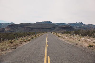 Empty country road passing through arid landscape against sky