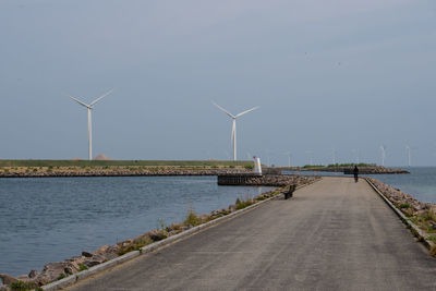 Windmills by sea against sky