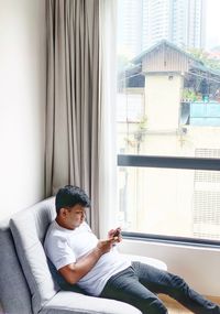 Man using smart phone while sitting on chair by window at home