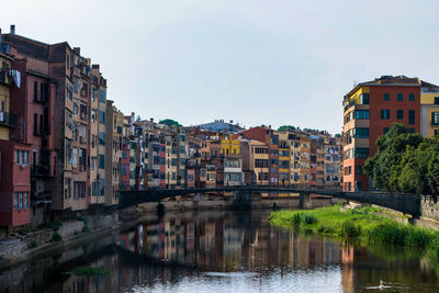 Buildings by river against sky in city, girona. 