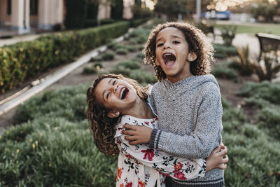 Cute siblings smiling and laughing while hugging outside in sunshine