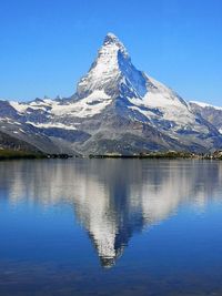 Scenic view of lake and snowcapped mountains against blue sky
