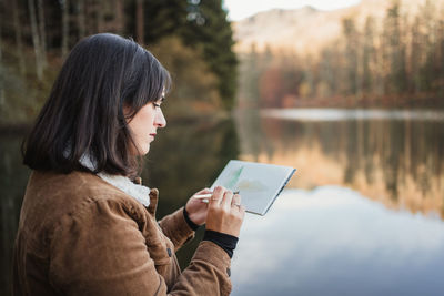 Side view of young woman looking away while standing on lake