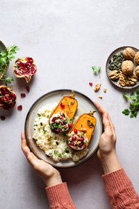 Top view of cropped unrecognizable person holding plate of delicious homemade rice and roasted pumpkins topped with pomegranates seeds placed on table in light kitchen on grey background