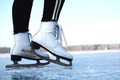 Low section of woman ice skating on rink against sky