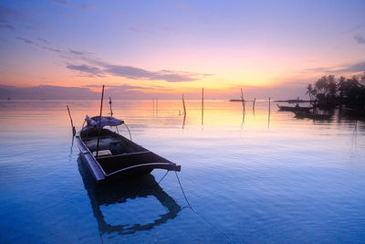 Sailboat moored on sea against sky during sunset