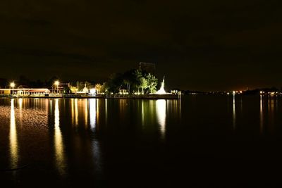 Illuminated buildings by lake against sky at night