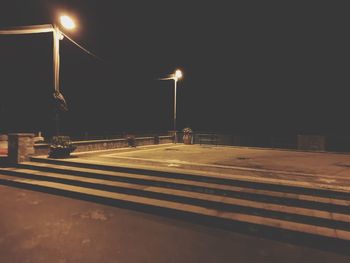 Empty road against illuminated street lights in city at night