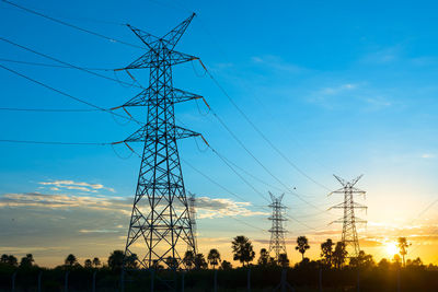 Low angle view of silhouette electricity pylons against sky during sunset