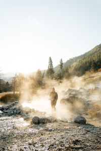 Woman walks through a cloud of fog and mist of a natural thermal hot spring in idaho 