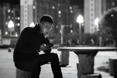 Man using phone on seat in city at night