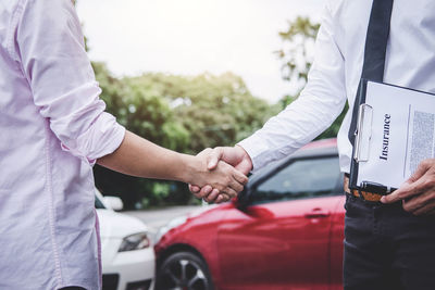 Midsection of man handshaking with insurance agent at parking lot