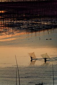 Silhouette fishing net on sea against sky during sunset