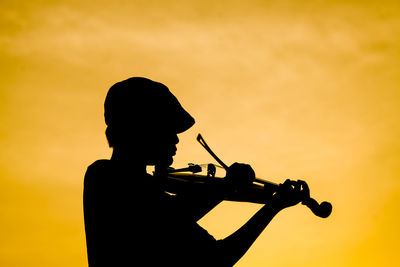 Silhouette boy playing violin against sky during sunset