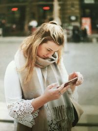 Young woman using mobile phone while standing on city street