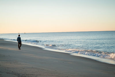 Man standing on beach against clear sky during sunset