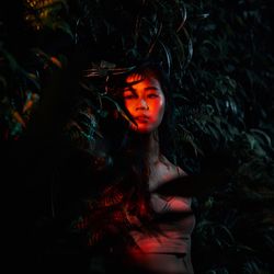 Thoughtful young woman standing by plants at night
