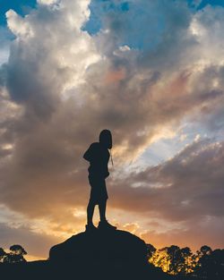 Silhouette man standing on rock against sky during sunset