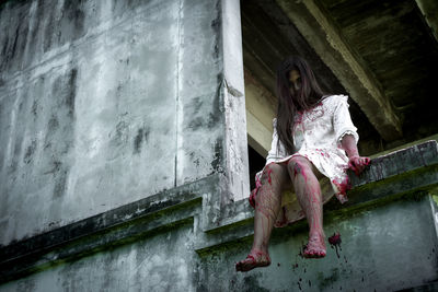 Low angle view of woman sitting on building wall during halloween
