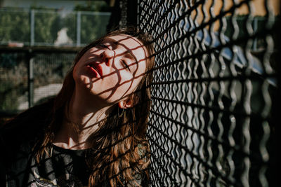 Portrait of young woman standing by chainlink fence