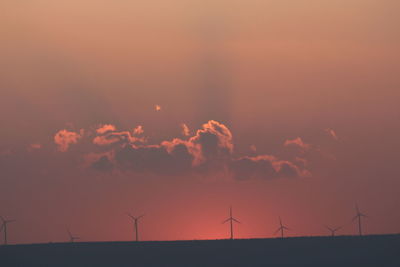 Silhouette of wind turbines on field against orange sky