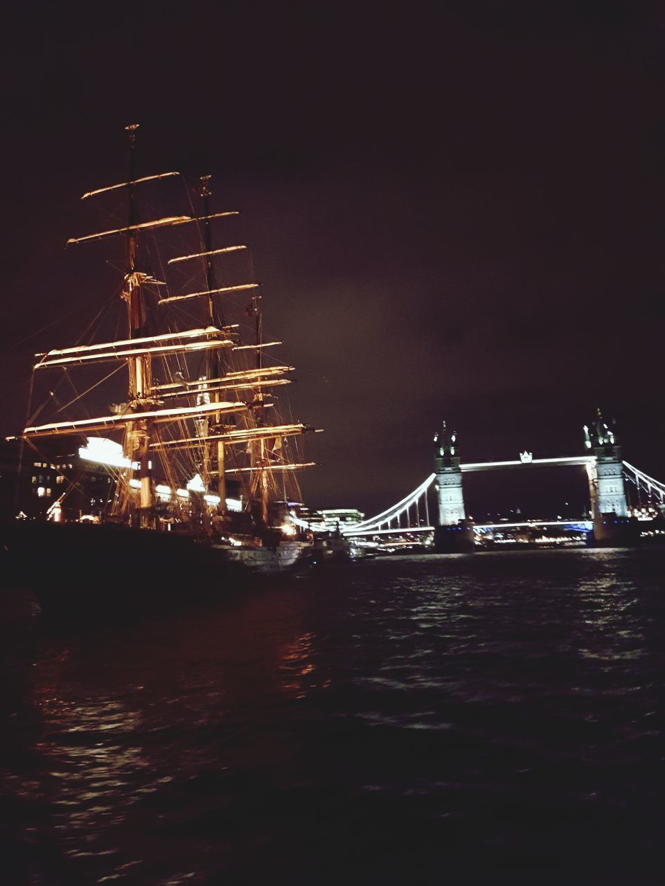 ILLUMINATED SUSPENSION BRIDGE OVER RIVER AGAINST SKY