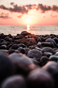 Close-up of pebbles on beach against sunset sky