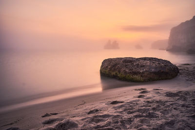 Rocks on beach against sky during sunset
