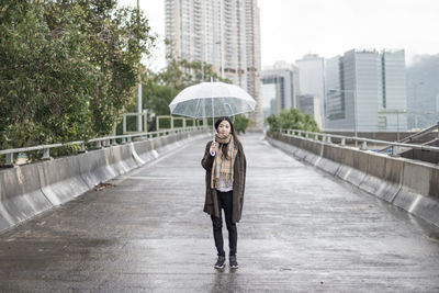 Woman with umbrella standing on wet road during rainy season