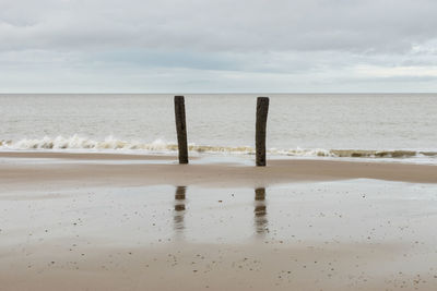 Wooden posts on beach against sky