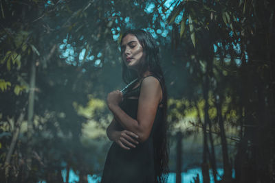 Young woman standing by trees in forest