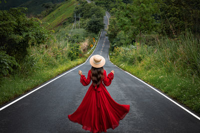 Rear view of woman wearing hat standing on road amidst plants