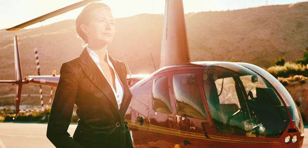 Businesswoman looking away while standing by helicopter during sunny day