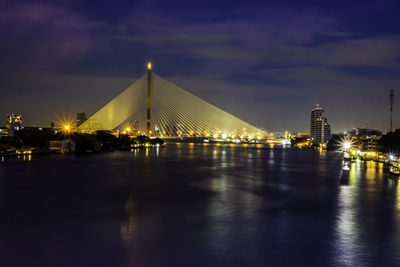 Illuminated buildings by river against sky at night